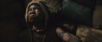Movie still from “Beasts of No Nation” (2015), directed by Cary Joji Fukunaga – A person wearing a hat and a necklace; Close Up shot, High angle
