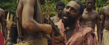 Movie still from “Beasts of No Nation” (2015), directed by Cary Joji Fukunaga – A man with a beard holding a rifle in his hand; Close Up shot, Over the shoulder angle
