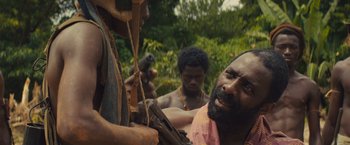 Movie still from “Beasts of No Nation” (2015), directed by Cary Joji Fukunaga – A group of men standing next to each other in a forest; Close Up shot, Over the shoulder angle