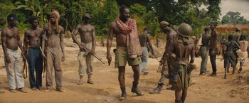 Movie still from “Beasts of No Nation” (2015), directed by Cary Joji Fukunaga – A group of men walking across a dirt field; Medium shot, Low angle