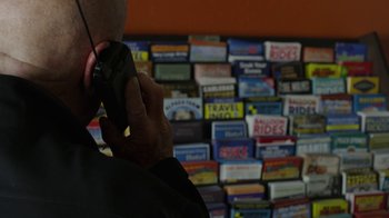 Movie still from “Better Call Saul” (2015), created by Vince Gilligan – A man is talking on a cell phone in front of a wall of cigarette boxes; Extreme Close Up shot, High angle