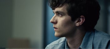 Movie still from “Black Mirror: Bandersnatch” (2018), directed by David Slade – A young man looking to his left while wearing a blue shirt; Close Up shot, Over the shoulder angle