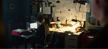 Movie still from “Black Mirror: Bandersnatch” (2018), directed by David Slade – A man sitting at a computer in front of papers on a desk; Wide shot, High angle