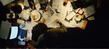 Movie still from “Black Mirror: Bandersnatch” (2018), directed by David Slade – A man sitting at a table with papers on it; Medium shot, Overhead angle