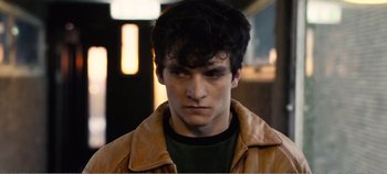 Movie still from “Black Mirror: Bandersnatch” (2018), directed by David Slade – A young man with dark hair wearing a brown jacket; Close Up shot, Over the shoulder angle