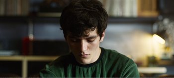 Movie still from “Black Mirror: Bandersnatch” (2018), directed by David Slade – A young man in a green t - shirt is looking down; Close Up shot, High angle