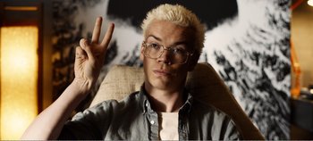 Movie still from “Black Mirror: Bandersnatch” (2018), directed by David Slade – A man with blonde spiky hair wearing glasses and making a peace sign with one hand; Close Up shot, High angle