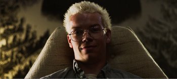 Movie still from “Black Mirror: Bandersnatch” (2018), directed by David Slade – A man with blonde hair and glasses sitting in a chair; Close Up shot, Low angle