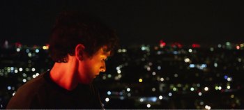 Movie still from “Black Mirror: Bandersnatch” (2018), directed by David Slade – A young man is looking at the lights of a city at night; Close Up shot, Over the shoulder angle