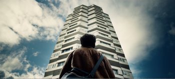 Movie still from “Black Mirror: Bandersnatch” (2018), directed by David Slade – A man standing in front of a tall building; Wide shot, Low angle