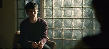 Movie still from “Black Mirror: Bandersnatch” (2018), directed by David Slade – A man sitting in front of a glass block window; Medium shot, Over the shoulder angle