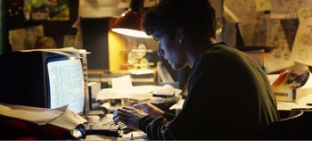 Movie still from “Black Mirror: Bandersnatch” (2018), directed by David Slade – A man sitting in front of a laptop computer; Medium shot, Low angle