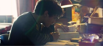 Movie still from “Black Mirror: Bandersnatch” (2018), directed by David Slade – A young man writing on top of an open book; Medium shot, Low angle