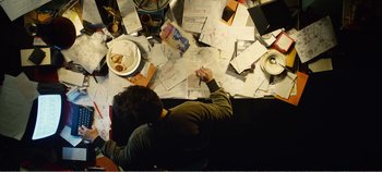 Movie still from “Black Mirror: Bandersnatch” (2018), directed by David Slade – A person sitting on a couch with a lot of papers on the floor; Medium shot, Overhead angle