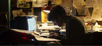 Movie still from “Black Mirror: Bandersnatch” (2018), directed by David Slade – A man writing on a piece of paper in front of a computer; Medium shot, Low angle