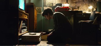 Movie still from “Black Mirror: Bandersnatch” (2018), directed by David Slade – A man sitting on the ground looking at a box; Medium shot, High angle