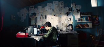 Movie still from “Black Mirror: Bandersnatch” (2018), directed by David Slade – A man sitting in front of a computer in front of a wall of papers; Medium shot, High angle