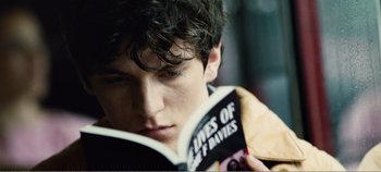Movie still from “Black Mirror: Bandersnatch” (2018), directed by David Slade – A young man reading a book in the rain; Close Up shot, High angle