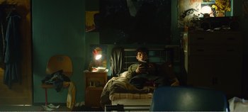 Movie still from “Black Mirror: Bandersnatch” (2018), directed by David Slade – A man sitting on a bed in a room with a lamp; Wide shot, Overhead angle