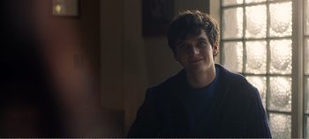 Movie still from “Black Mirror: Bandersnatch” (2018), directed by David Slade – A young man smiling for the camera in a dark room; Close Up shot, Over the shoulder angle