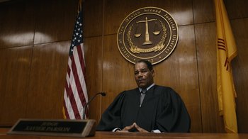 Movie still from “Better Call Saul” (2015), created by Vince Gilligan – A judge in a courtroom with a flag in the background; Medium shot, Low angle