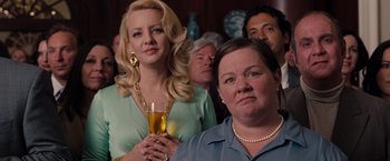 Movie still from “Bridesmaids” (2011), directed by Paul Feig – A woman holding a glass of wine in front of other people; Close Up shot, Over the shoulder angle