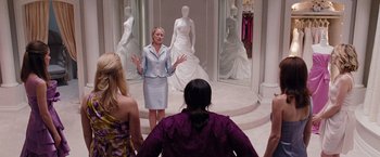 Movie still from “Bridesmaids” (2011), directed by Paul Feig – A group of people standing around a room with dresses on display; Wide shot, Over the shoulder angle