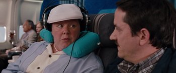 Movie still from “Bridesmaids” (2011), directed by Paul Feig – A man and a woman sitting on a plane wearing headphones; Close Up shot, Over the shoulder angle