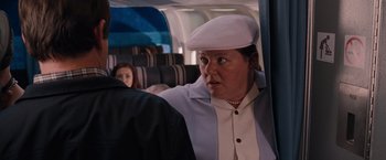 Movie still from “Bridesmaids” (2011), directed by Paul Feig – A woman in a white hat is sitting on a plane; Medium shot, Over the shoulder angle