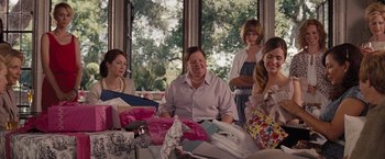 Movie still from “Bridesmaids” (2011), directed by Paul Feig – A group of people sitting around a table with a lot of gifts; Medium shot, Over the shoulder angle