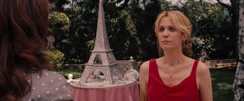 Movie still from “Bridesmaids” (2011), directed by Paul Feig – A woman standing next to a cake shaped like the eiffel tower; Medium shot, Over the shoulder angle