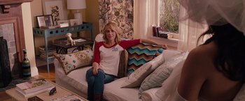 Movie still from “Bridesmaids” (2011), directed by Paul Feig – A woman sitting on top of a couch in a living room; Medium shot, Over the shoulder angle