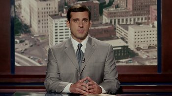 Movie still from “Bruce Almighty” (2003), directed by Tom Shadyac – A man in a suit and tie sitting in front of a news desk; Medium shot, Over the shoulder angle