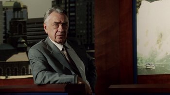 Movie still from “Bruce Almighty” (2003), directed by Tom Shadyac – An older man wearing a suit and tie sitting in a chair; Medium shot, Over the shoulder angle