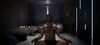 Movie still from “Chambers” (2019), created by Leah Rachel – A man sitting on the ground in a yoga pose; Medium shot, High angle