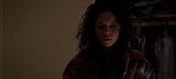 Movie still from “Chambers” (2019), created by Leah Rachel – A woman with curly hair is standing in the dark; Close Up shot, High angle