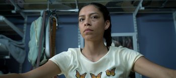 Movie still from “Chambers” (2019), created by Leah Rachel – A young woman wearing a white t - shirt with butterflies on it; Close Up shot, Low angle