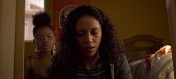 Movie still from “Chambers” (2019), created by Leah Rachel – A woman with curly hair is sitting in a room; Close Up shot, Over the shoulder angle