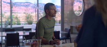 Movie still from “Chambers” (2019), created by Leah Rachel – A man sitting at a table with a cup in his hand; Medium shot, Over the shoulder angle