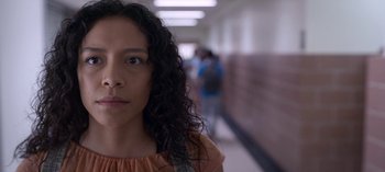 Movie still from “Chambers” (2019), created by Leah Rachel – A woman with long black curly hair standing in a school hallway; Close Up shot, Low angle