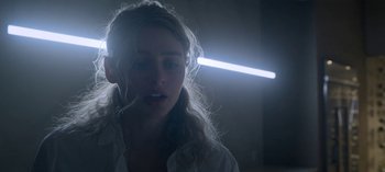 Movie still from “Chambers” (2019), created by Leah Rachel – A woman with a light in the background; Close Up shot, Low angle