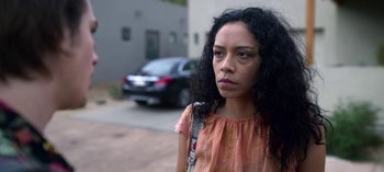 Movie still from “Chambers” (2019), created by Leah Rachel – A young woman with long black curly hair wearing an orange dress; Close Up shot, Low angle
