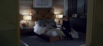 Movie still from “Chambers” (2019), created by Leah Rachel – A woman sitting on top of a bed reading a book; Wide shot, High angle