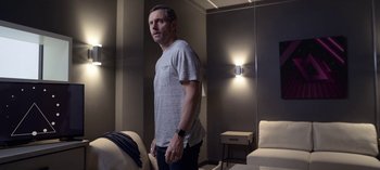 Movie still from “Chambers” (2019), created by Leah Rachel – A man standing in a living room with his hands in his pockets; Medium shot, Over the shoulder angle