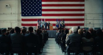 Movie still from “Charlie Wilson's War” (2007), directed by Mike Nichols – A crowd of people sitting in front of an american flag; Extreme Wide shot, High angle