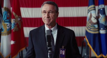Movie still from “Charlie Wilson's War” (2007), directed by Mike Nichols – A man in a suit and tie holding a microphone in front of an american flag; Close Up shot, Low angle