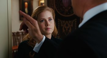 Movie still from “Charlie Wilson's War” (2007), directed by Mike Nichols – A woman in a black suit and white shirt is looking at a man in a black suit and white shirt in front of a wall; Close Up shot, Over the shoulder angle