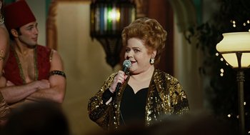 Movie still from “Charlie Wilson's War” (2007), directed by Mike Nichols – A woman in a black top is singing into a microphone; Medium shot, Over the shoulder angle