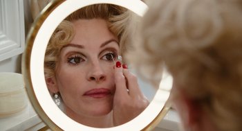 Movie still from “Charlie Wilson's War” (2007), directed by Mike Nichols – A woman looking in the mirror while putting lipstick on her face; Close Up shot, Over the shoulder angle