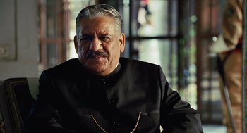 Movie still from “Charlie Wilson's War” (2007), directed by Mike Nichols – An older man in a black suit and gold chain; Close Up shot, Low angle